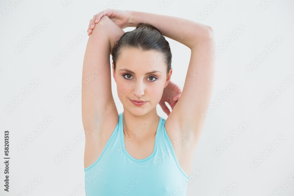Toned woman stretching hands behind head against wall Toned woman stretching hands behind head against wall