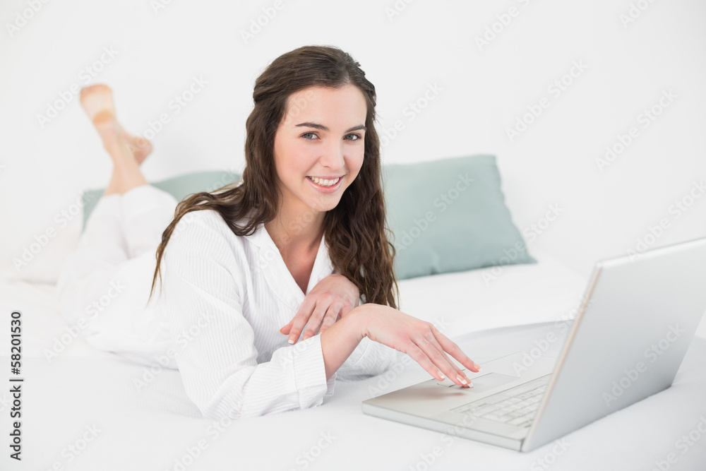 Relaxed smiling casual brunette using laptop in bed Relaxed smiling casual brunette using laptop in bed