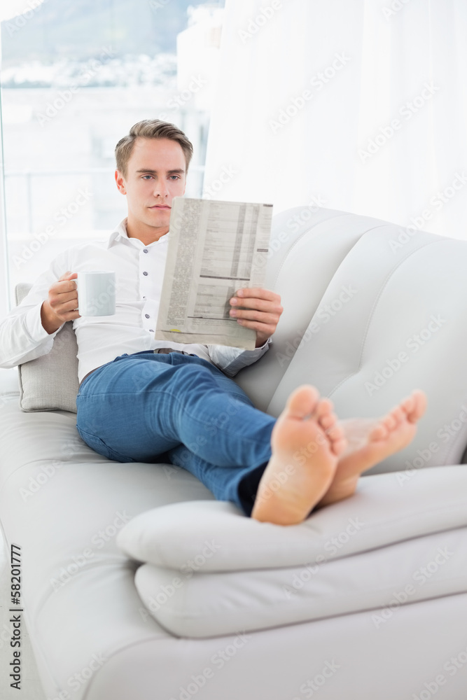 Relaxed man with coffee cup while reading newspaper on sofa Relaxed man with coffee cup while reading newspaper on sofa