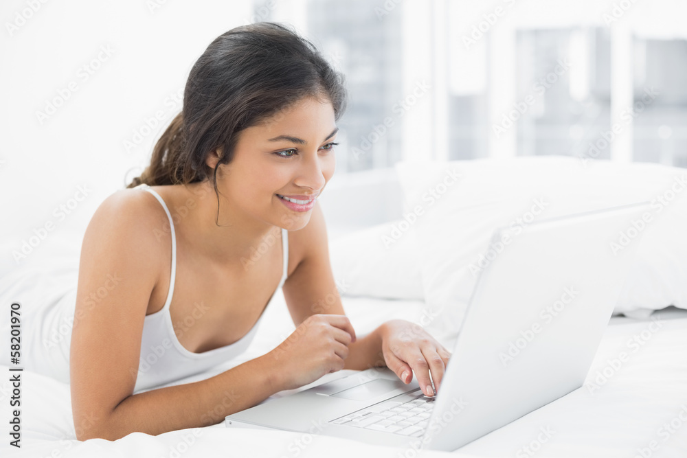 Smiling casual young woman using laptop in bed Smiling casual young woman using laptop in bed