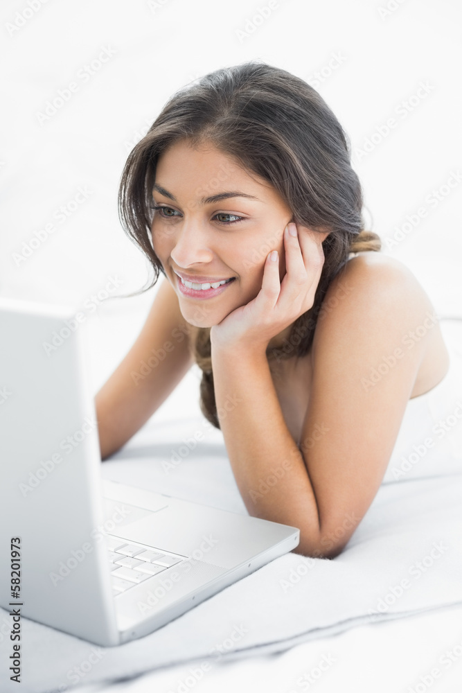 Smiling casual woman using laptop in bed