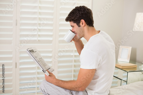 Man drinking coffee while reading newspaper in bed