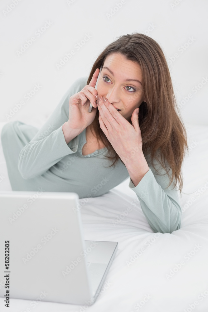 Shocked casual woman using cellphone and laptop in bed Shocked casual woman using cellphone and laptop in bed