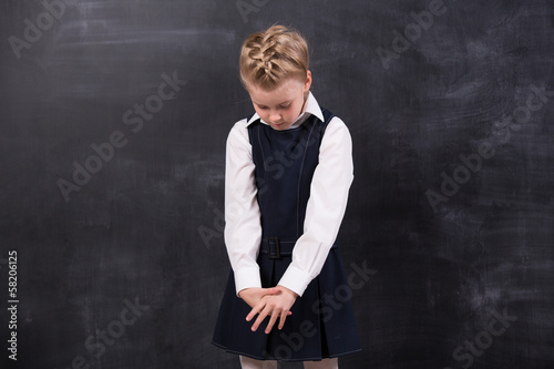 Sad little schoolgirl near blackboard