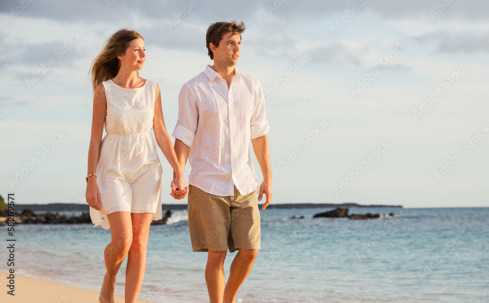Romantic happy couple walking on beach at sunset. Smiling holdin