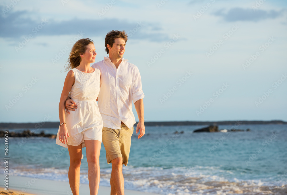 Romantic happy couple walking on beach at sunset. Smiling holdin