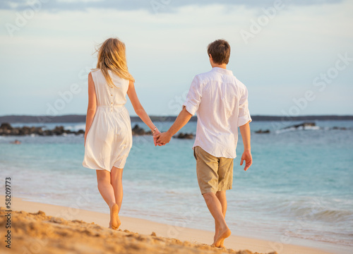 Romantic happy couple walking on beach at sunset. Smiling holdin