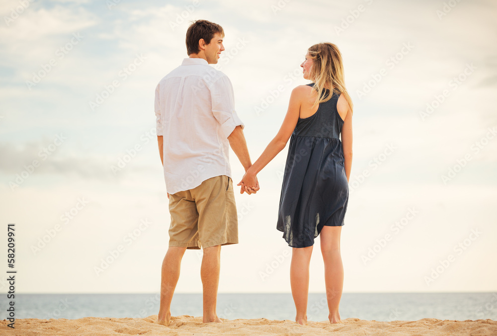 Romantic happy couple on beach at sunset. Smiling holding hands.
