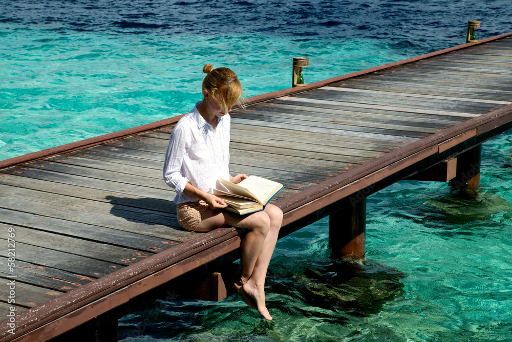 Girl reads a book while sits on a pier
