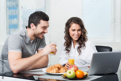 beautiful couple having breakfast with a laptop