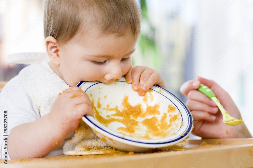 Sweet messy baby boy biting plate after eating the food. Sweet messy baby boy biting plate after eating the food.