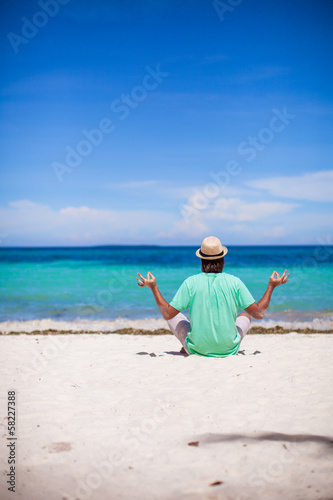 Young man sitting in lotus position on white tropical beach © travnikovstudio