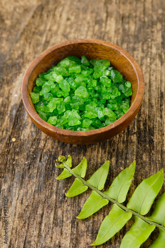 Green salt in bowl and fern leaf on old wooden