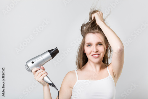 ttractive teenager blow drying her hair and looking at camera photo