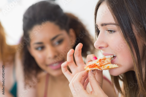 Young female eating pizza with blurred friends at home
