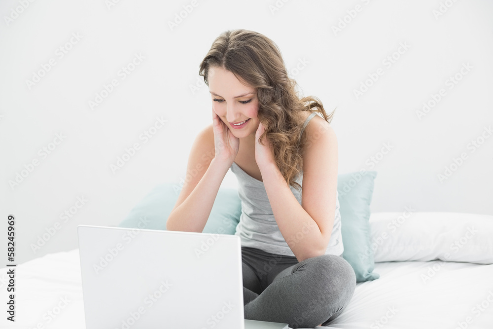 Smiling casual brunette looking at laptop in bed Smiling casual brunette looking at laptop in bed