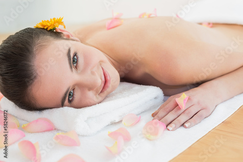 Beautiful woman resting on towel with petals at beauty spa