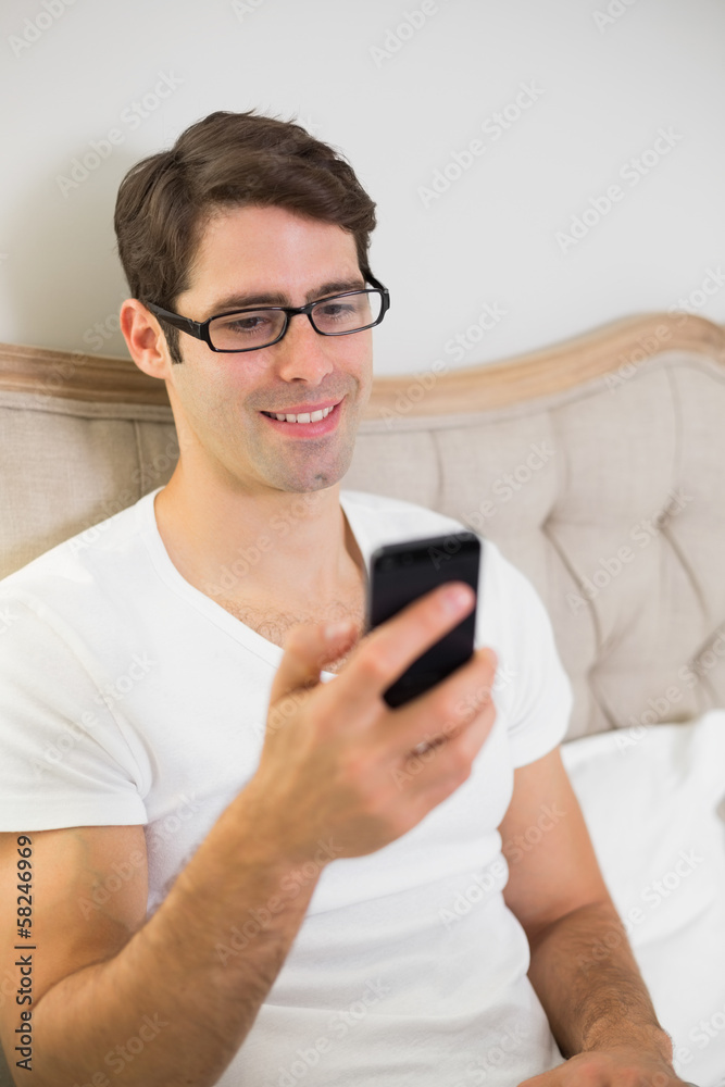 Casual smiling young man text messaging in bed Casual smiling young man text messaging in bed
