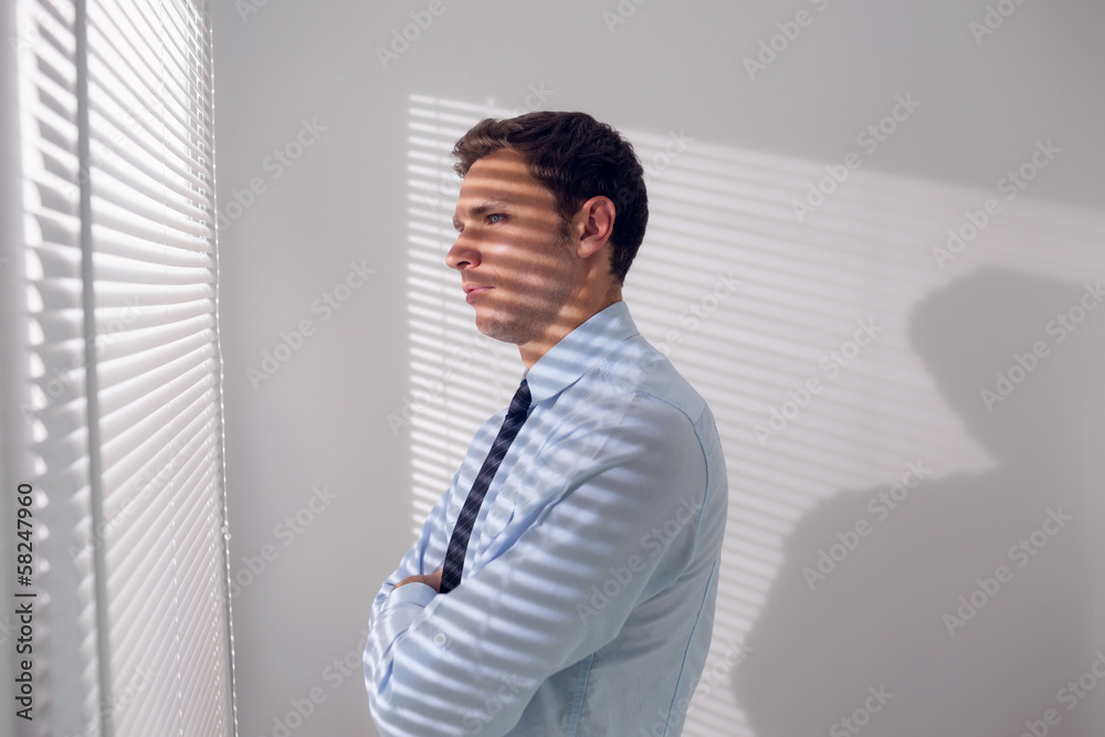Businessman peeking through blinds in office Businessman peeking through blinds in office