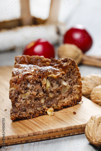 Cinnamon cake on wooden tray. Red apples and nuts in the back