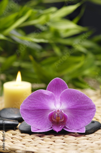 orchid and stones with candle, green leaf on wicker mat