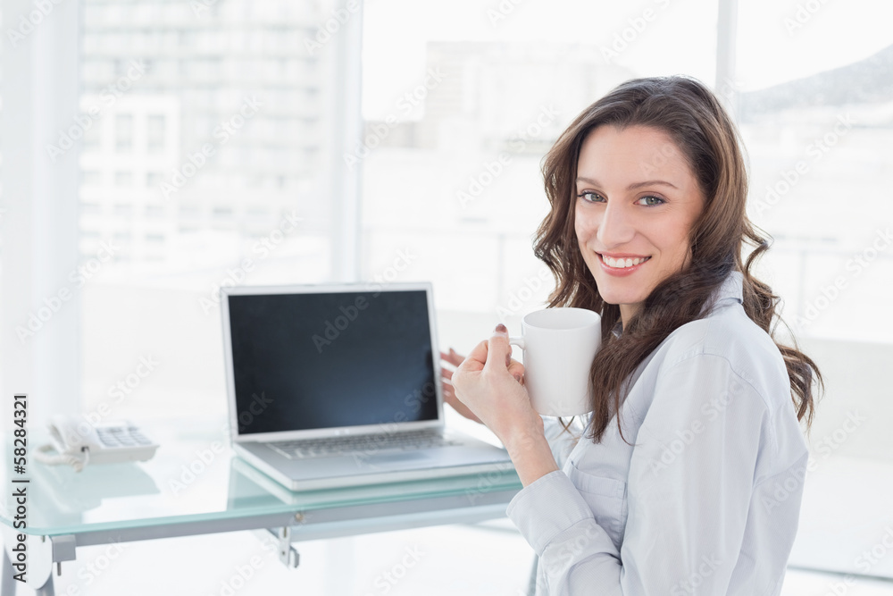 Businesswoman with coffee cup in front of laptop in office Businesswoman with coffee cup in front of laptop in office