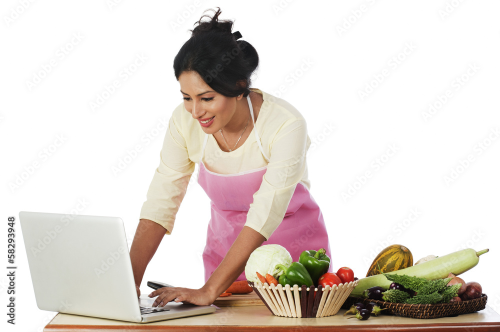 Woman cutting vegetables and using a laptop Woman cutting vegetables and using a laptop