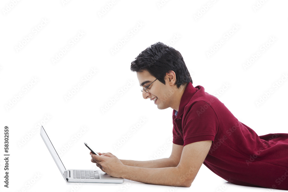 Man lying in front of a laptop and using a mobile phone Man lying in front of a laptop and using a mobile phone