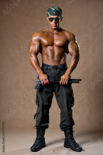 A muscular man with a gun in full view. © kanzefar