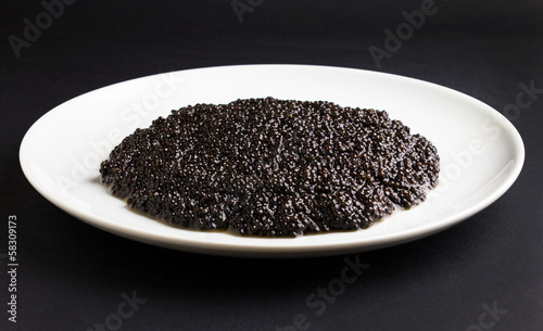 Black caviar in a white plate on black surface