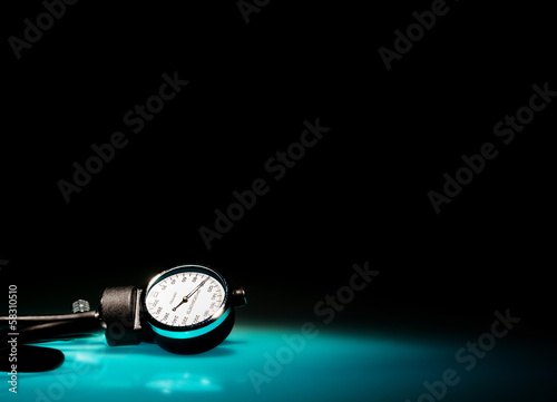 Sphygmomanometer on blue, reflective table and black background