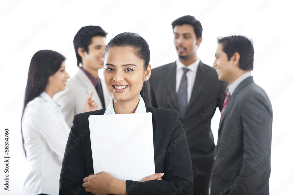 Portrait of a businesswoman smiling with her colleagues in the background Portrait of a businesswoman smiling with her colleagues in the background