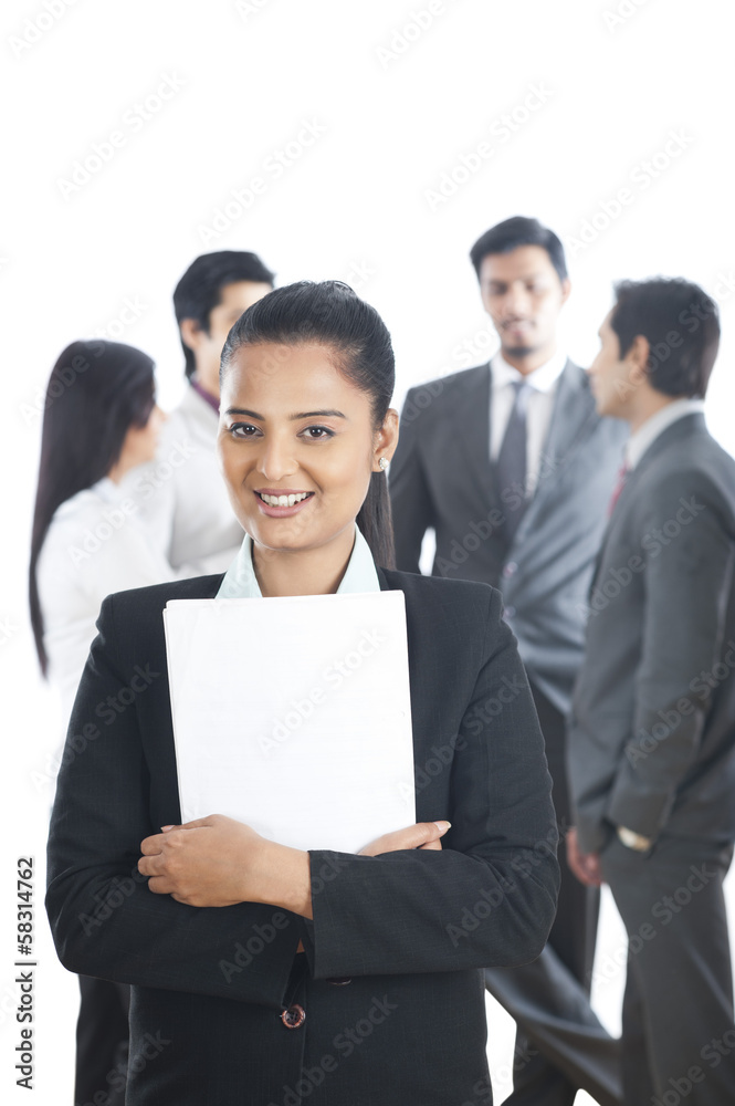 Portrait of a businesswoman smiling with her colleagues in the background Portrait of a businesswoman smiling with her colleagues in the background