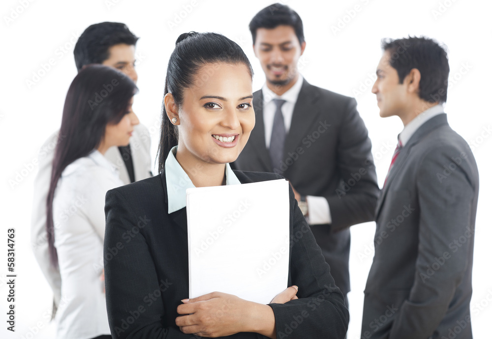 Portrait of a businesswoman smiling with her colleagues in the background Portrait of a businesswoman smiling with her colleagues in the background
