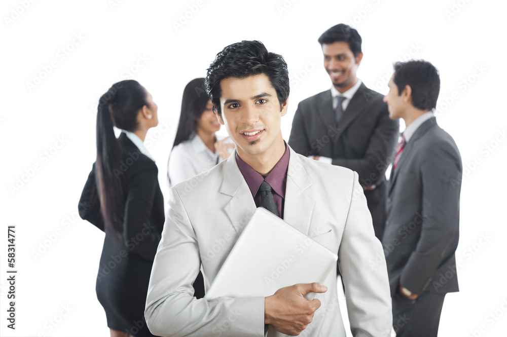 Portrait of a businessman smiling with his colleagues in the background Portrait of a businessman smiling with his colleagues in the background