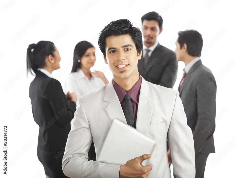 Portrait of a businessman smiling with his colleagues in the background Portrait of a businessman smiling with his colleagues in the background