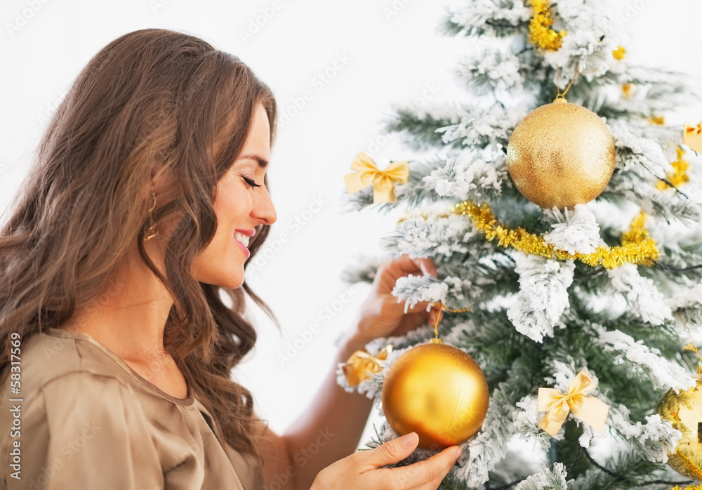 Naklejka premium Happy young woman decorating christmas tree with christmas ball