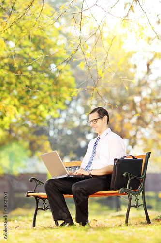Young businessperson on a bench working on a laptop in a park © Ljupco Smokovski