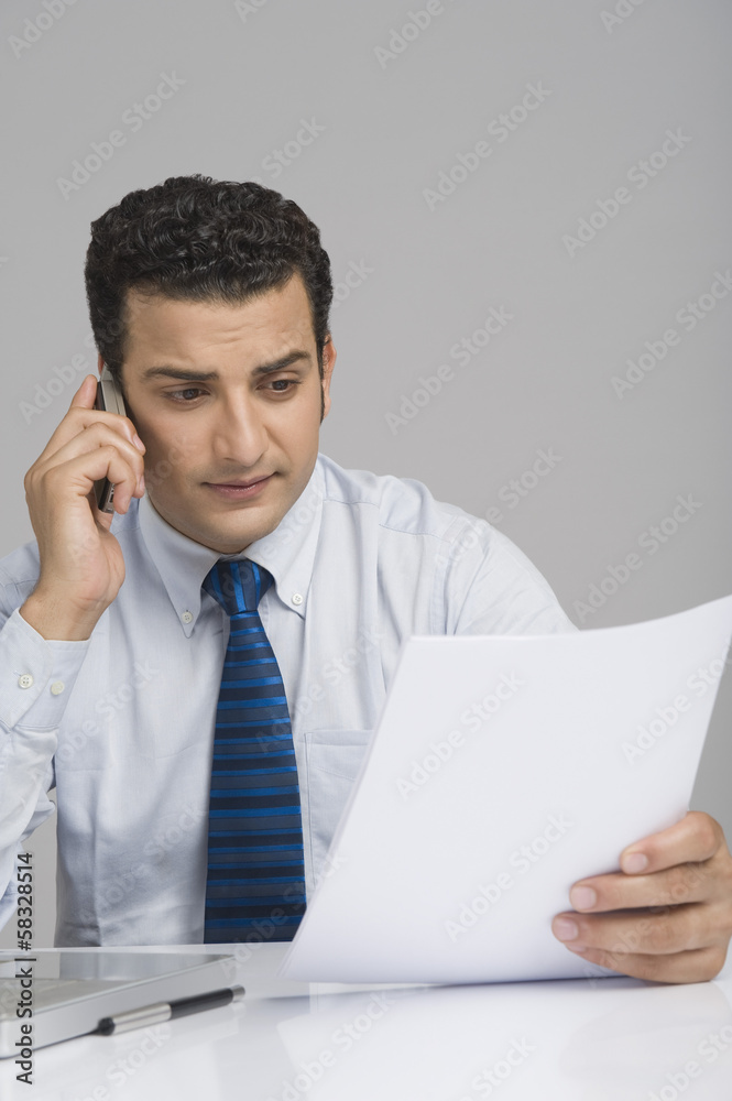 Businessman holding a document and talking on a mobile phone Businessman holding a document and talking on a mobile phone