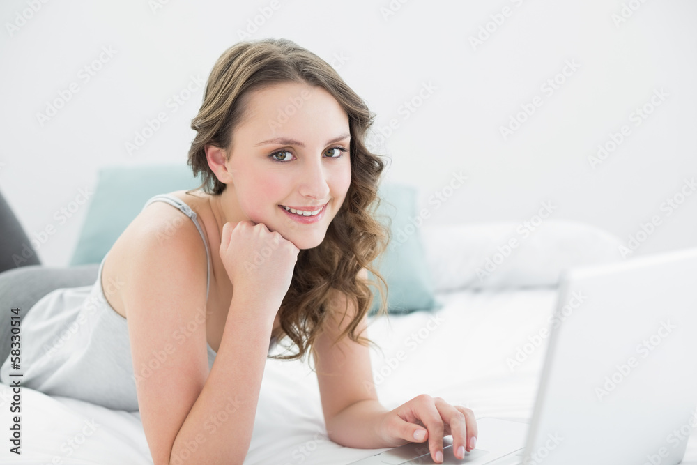 Smiling casual brunette using laptop in bed Smiling casual brunette using laptop in bed