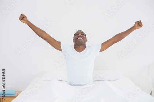 Smiling Afro man stretching his arms out in bed