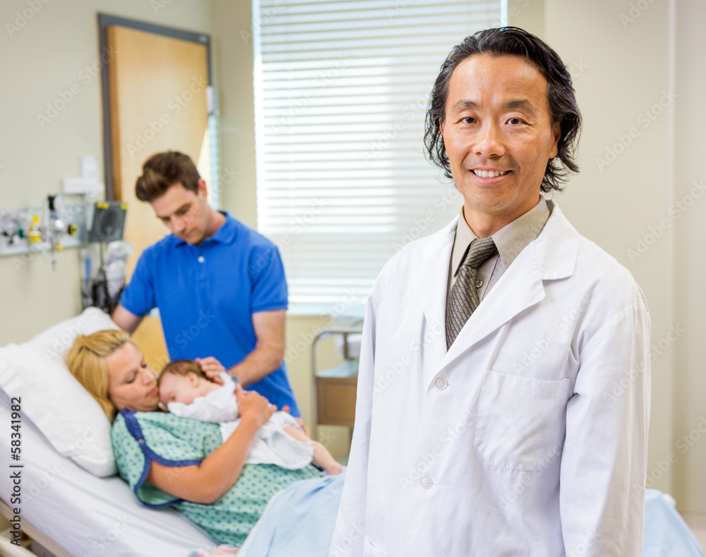Mature Doctor Standing With Couple And Newborn Baby In Backgroun Mature Doctor Standing With Couple And Newborn Baby In Backgroun