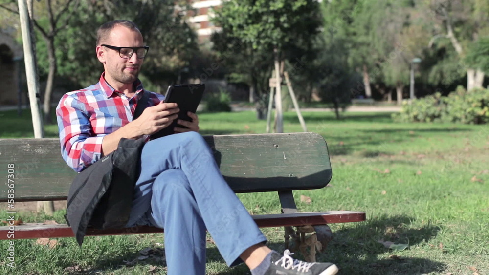 Young man browsing on tablet sitting on bench in the park Young man browsing on tablet sitting on bench in the park