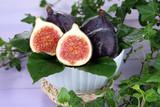 Ripe figs in bowl in leaves on wooden table close-up