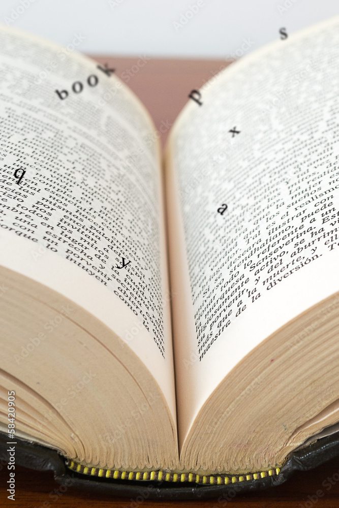 Fototapeta premium Old open book with magic falling letters on wood