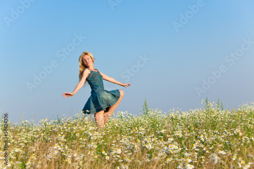 The happy young woman jumps in the field of camomiles..