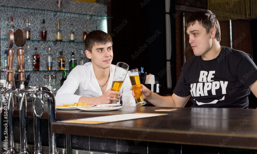 Two young men toasting each other over a beer