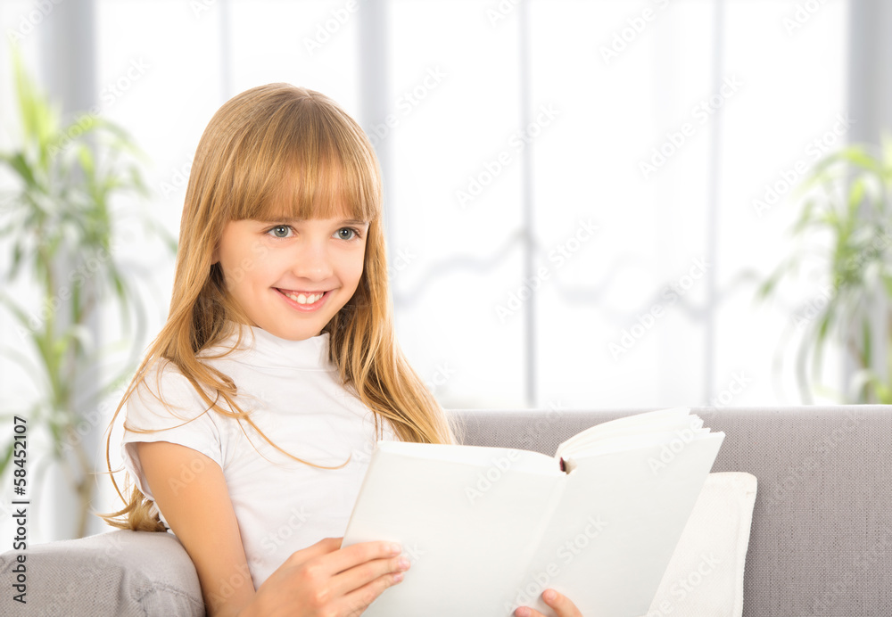 happy child girl reading a book while sitting on sofa happy child girl reading a book while sitting on sofa
