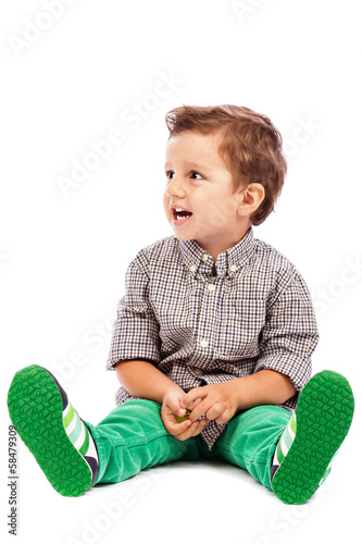 Adorable little boy sitting on the floor and looking at somethin photo