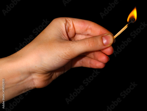 Burning match in hand on black background